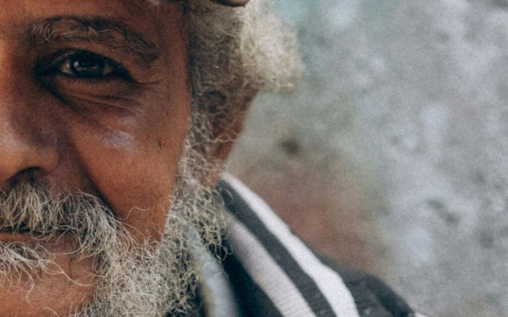 vieil homme défavorisé avec une barbe le teint doré vêtu d'une chemise à rayure blanches et noir et d'une casquette