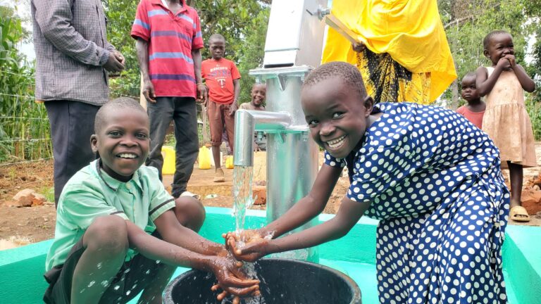 Petite fille et petit garçons souriant mettant les mains sous l'arrivée d'eau d'un puits creusé par Save ONG